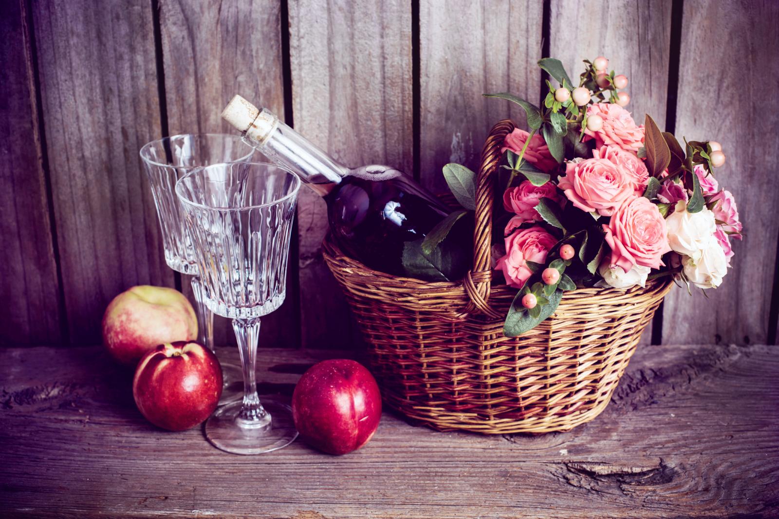 cesta de mimbre y una botella de vino rosado con dos copas y nectarinas 