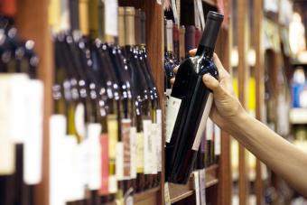La mano de una mujer se extiende para seleccionar una botella de vino tinto.