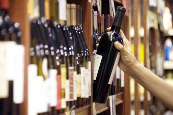 La mano de una mujer se extiende para seleccionar una botella de vino tinto. 